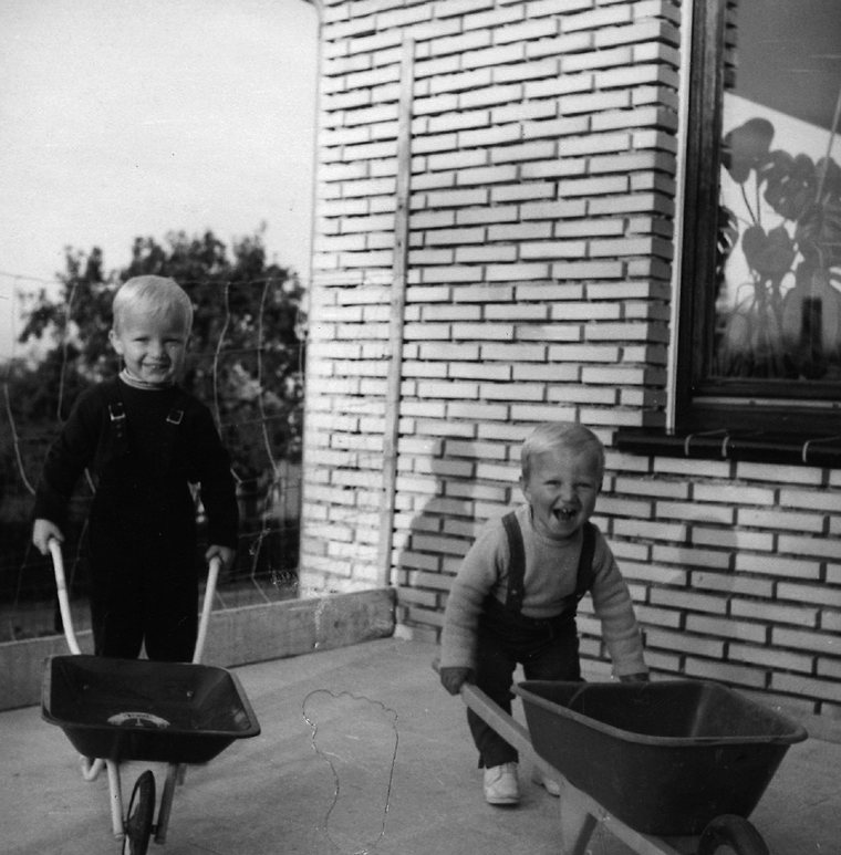 Deux jeunes enfants poussant des brouettes devant une maison en briques, photo d'archive